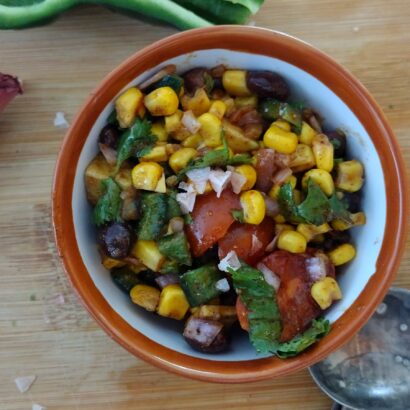 Bowl of summer corn salad with shallot, knife, measuring spoons and poblano in the background.
