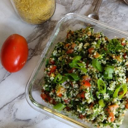 Dish of tabouli salad with tomato, bulgur and lime peel in background.