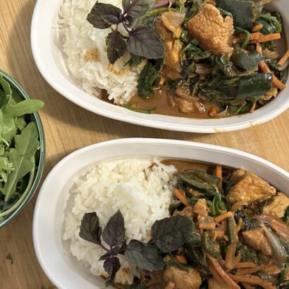 Two dishes of coconut chicken curry with rice. Bowl of greens to the left.