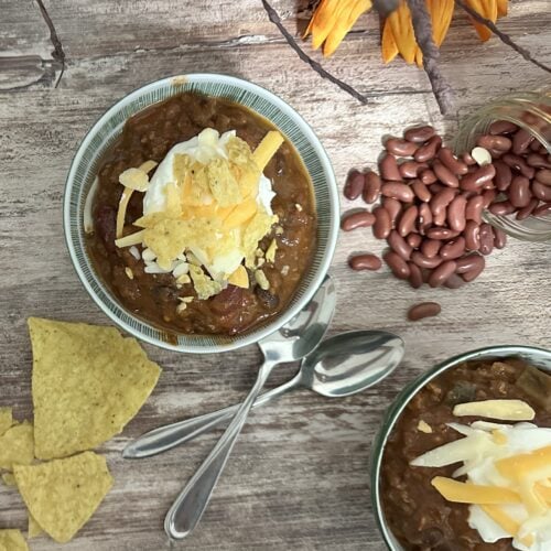 Two bowls of chili with sour cream, cheese and chips.