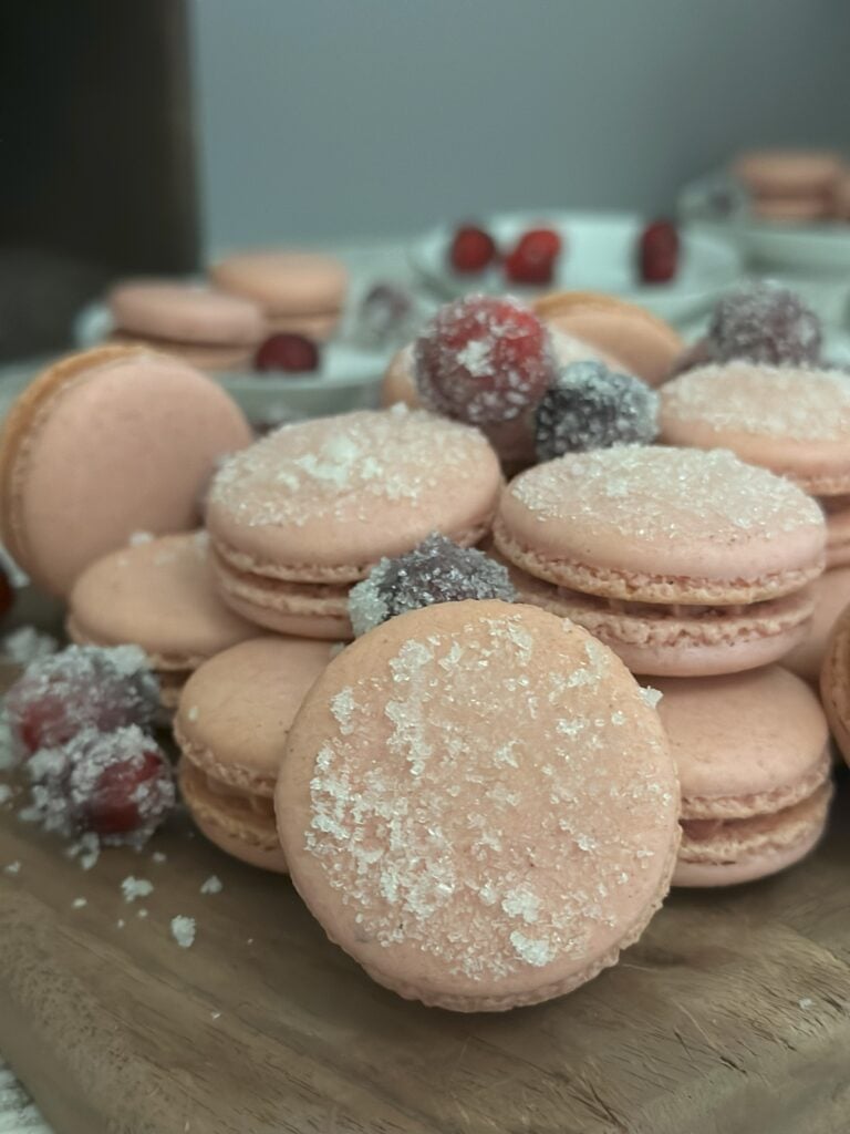 Cranberry spice macarons stacked on top of each other with sugared cranberries.