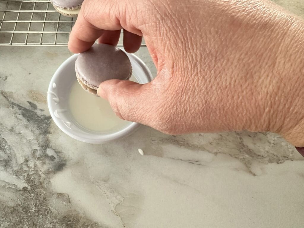 Demonstrating how to dip the macaron in the icing.