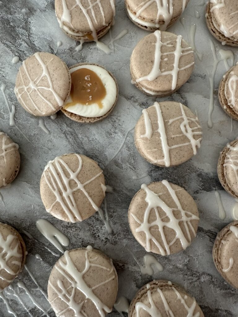 Salted caramel French macarons spread on a counter top, one macaron with the top off showing the filling inside.