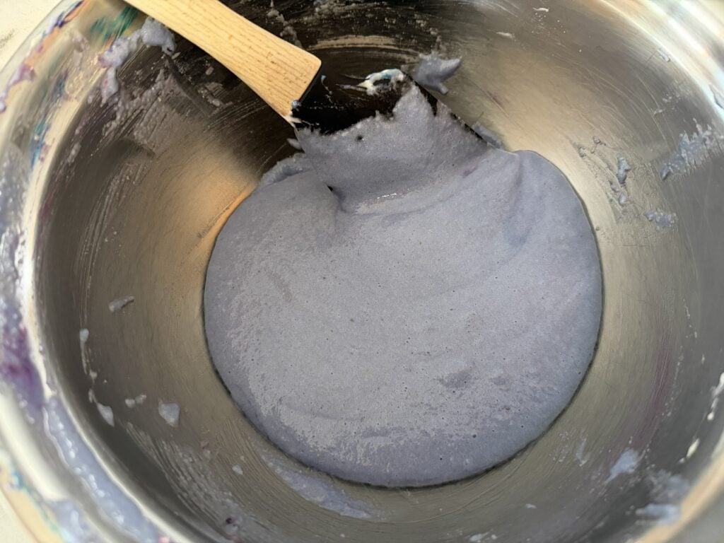 Using spatula to scrape underneath macaronage to help make a cohesive batter.