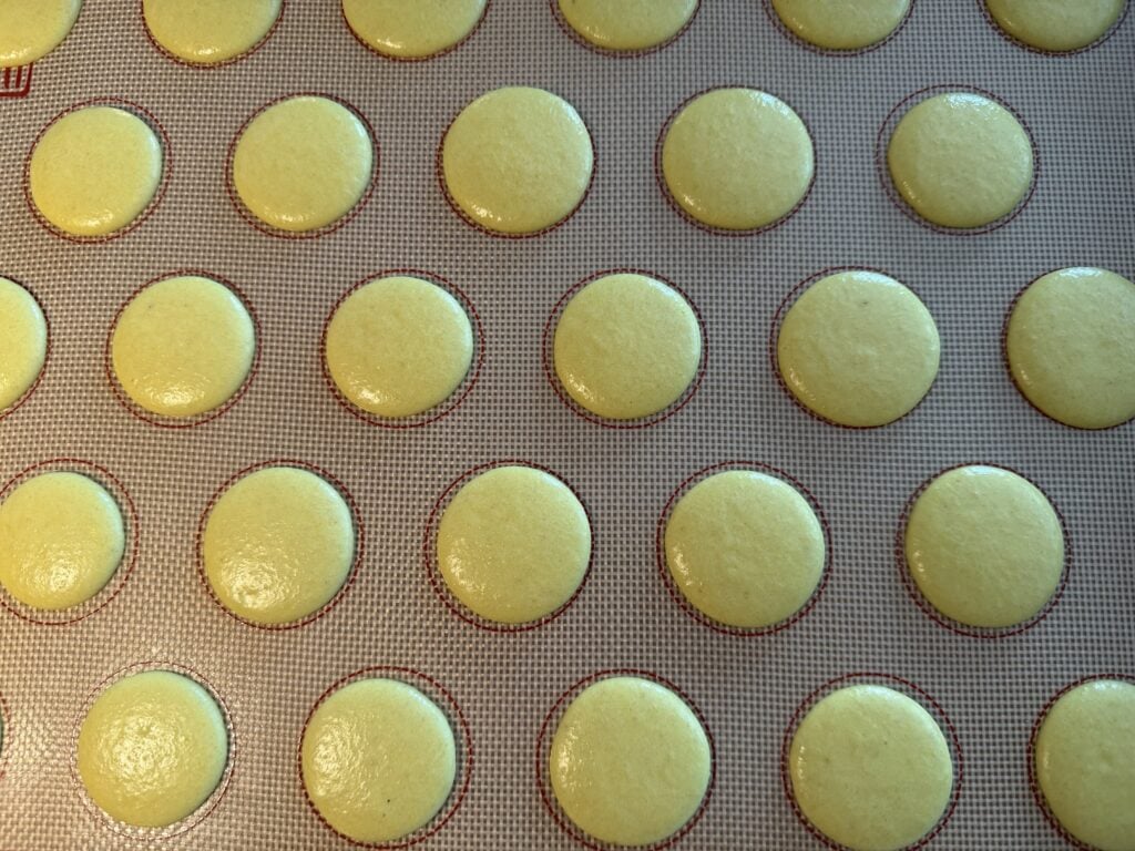 Piped lemon macaron batter onto a silicone mat.