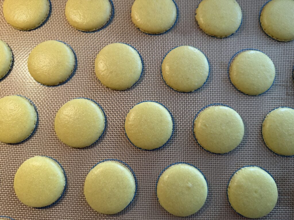 Baked lemon macaron shells on a silicone mat.