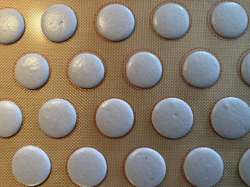 Purple macarons shells piped onto silicone mat.