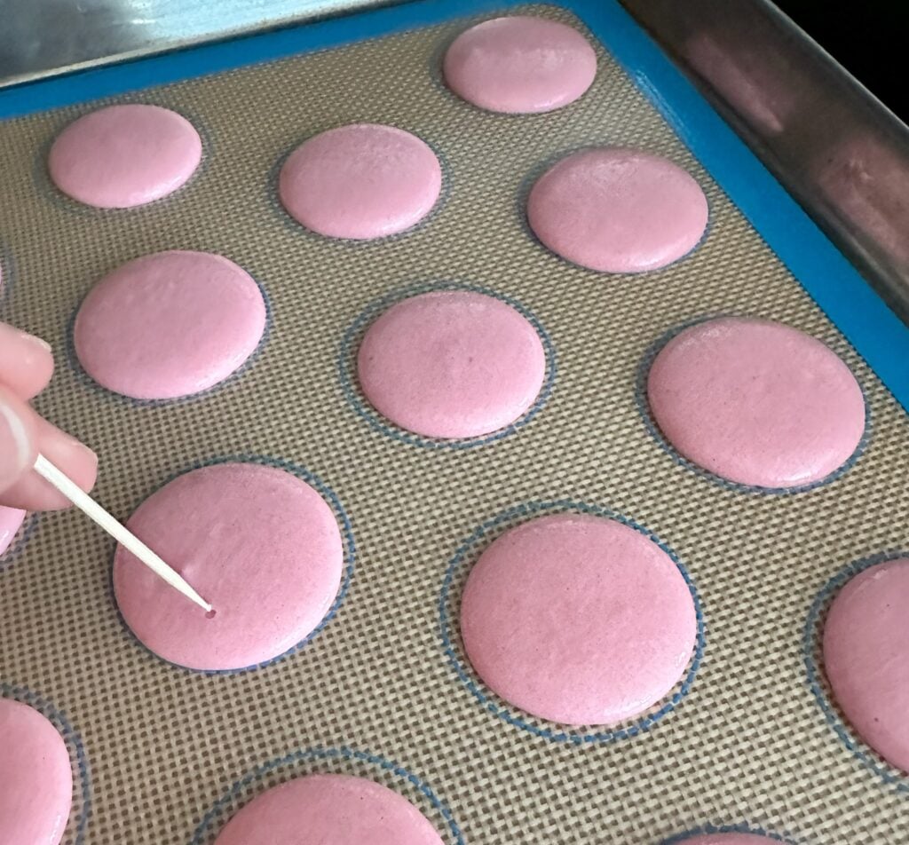 Using a toothpick to pop small air bubbles in the macaron shells.
