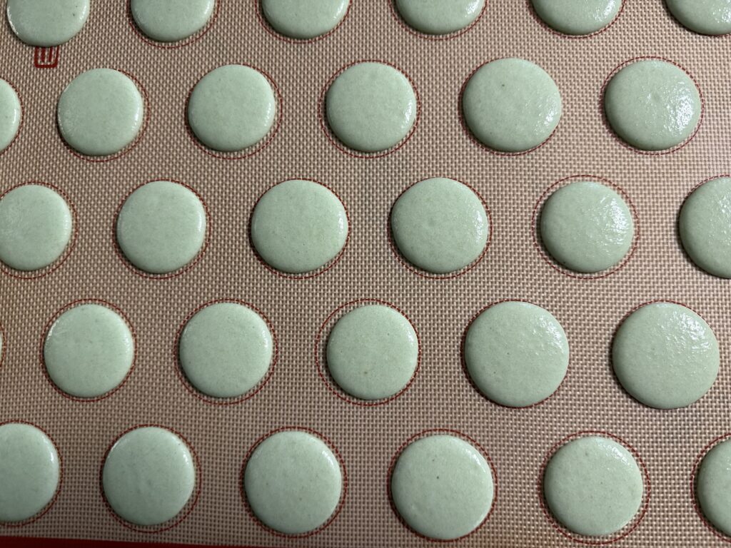 Pistachio macaron shells piped onto a silicone mat.