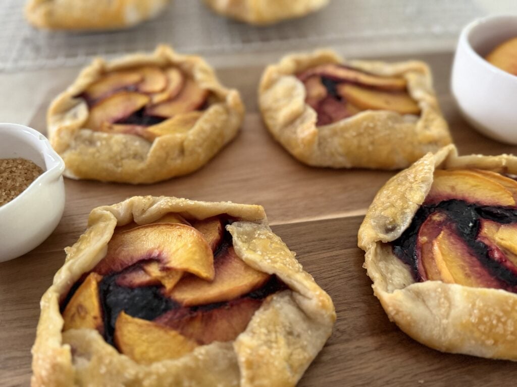 Four peach blueberry mini galettes on a cutting board.