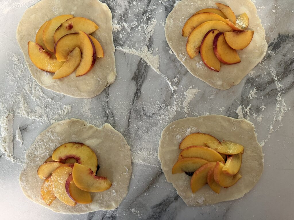 Blueberry compote underneath peach slices on four circles of pie dough.