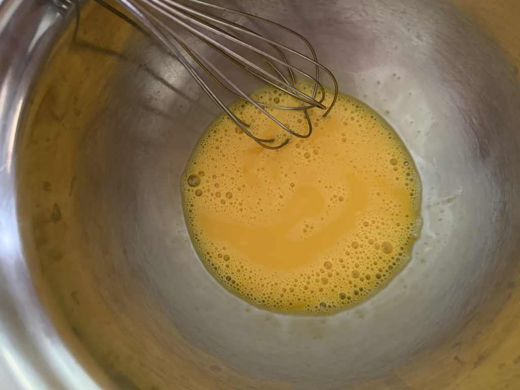 Eggs whisked until frothy in a bowl.