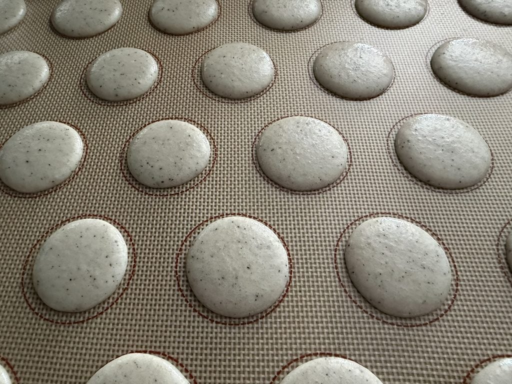 Coffee macaron shells piped onto a silicone mat.
