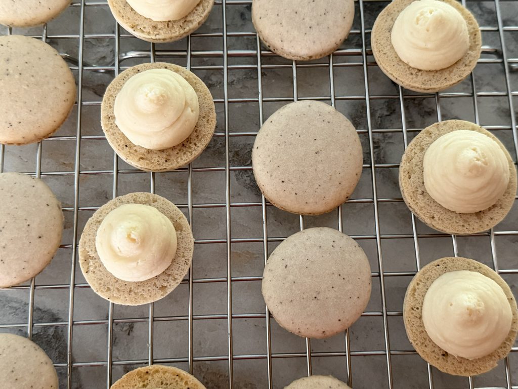 Tiramisu macarons with espresso mascarpone filling piped onto one shell and a second shell flipped upside down beside it.